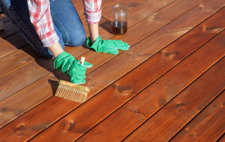 Person applying protective oil to a Fijian mahogany deck using a wide brush, ensuring durability and rich color.